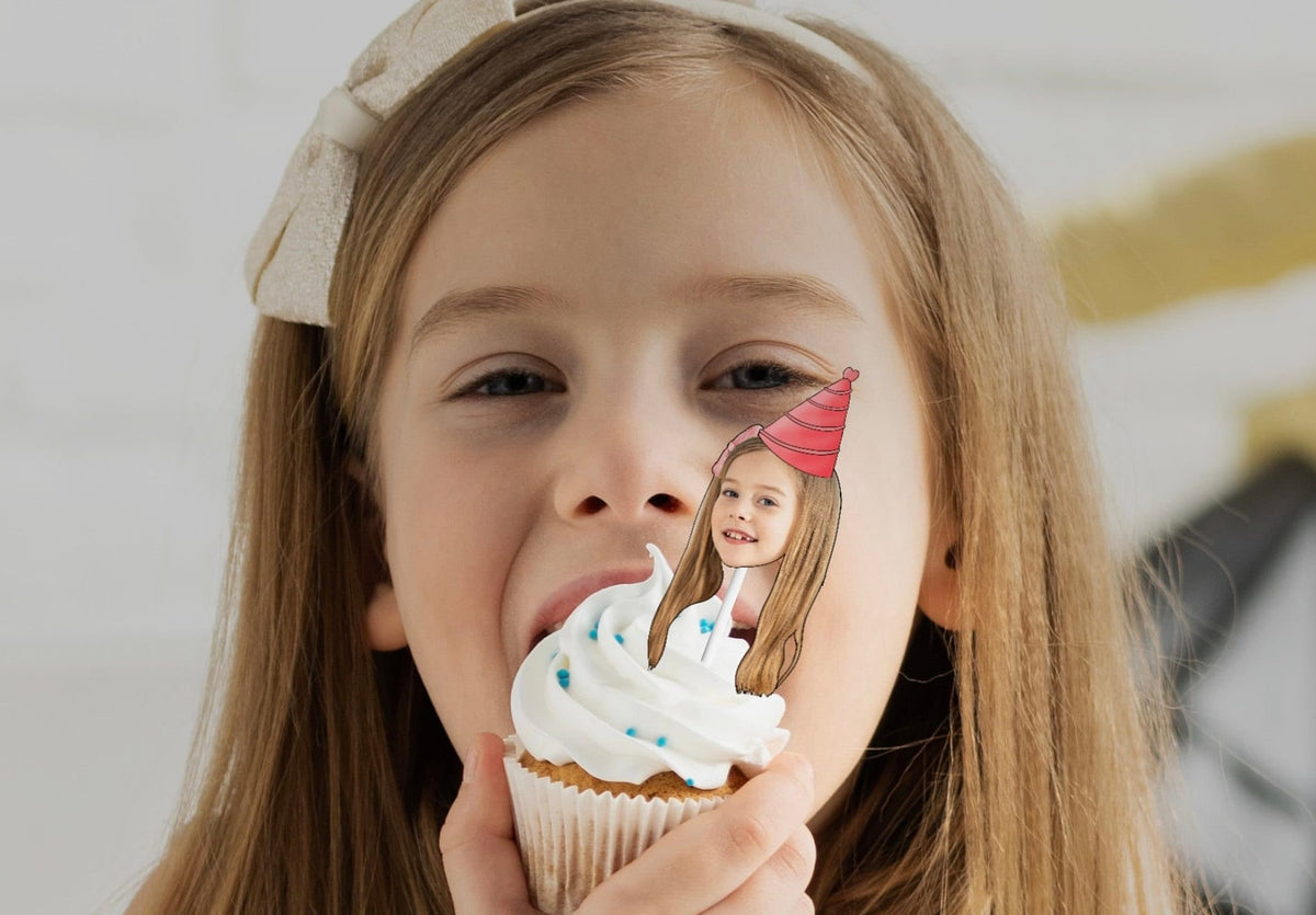 A festive decoration featuring a cut-out of a person's head wearing a colorful party hat, placed on top of a delicious cupcake, perfect for a birthday celebration.