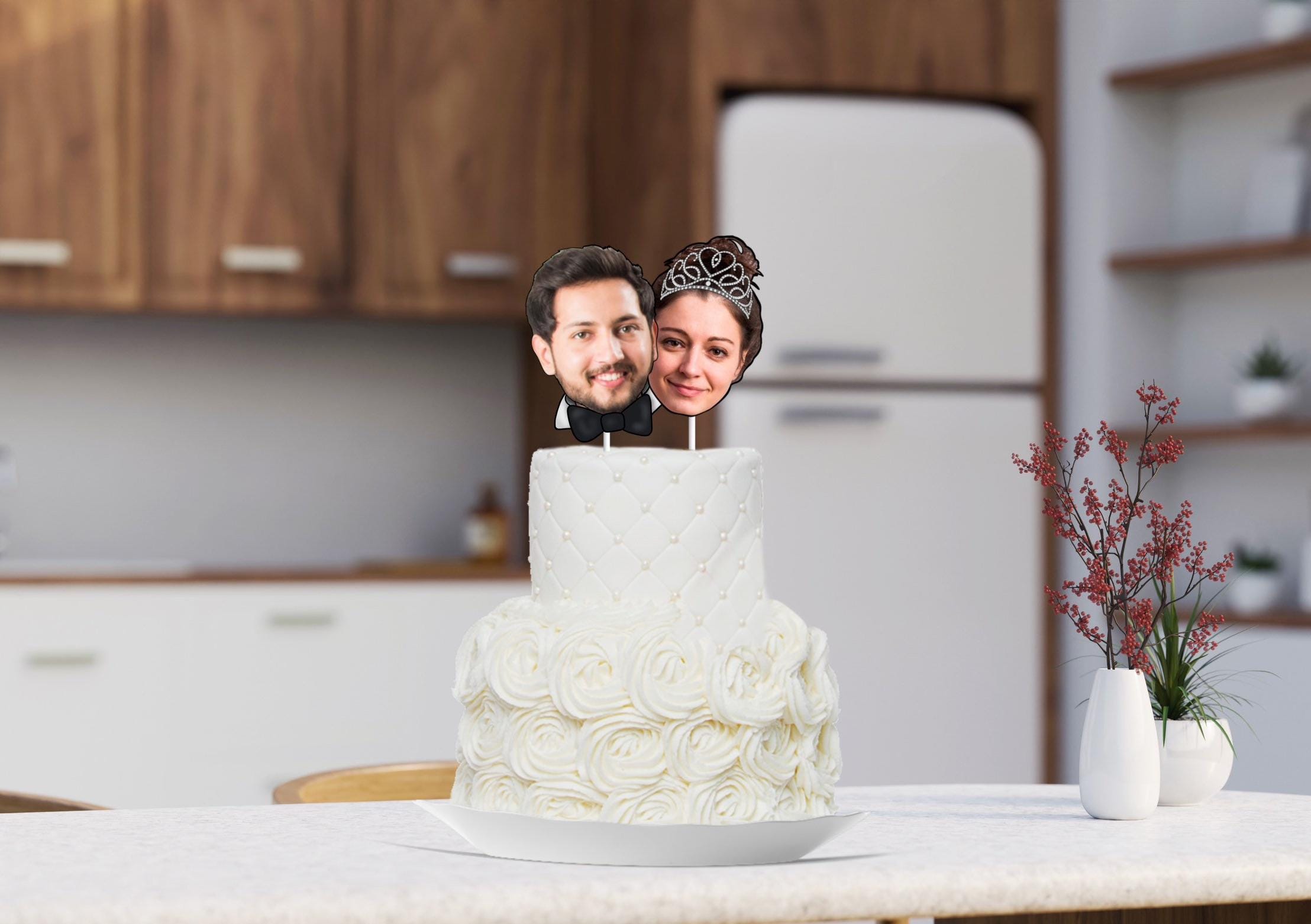 A personalized cake topper featuring a groom and bride, with their heads cut out from a photo. The groom is wearing a bow tie, while the bride is wearing a tiara, adding a unique and celebratory touch to the cake.
