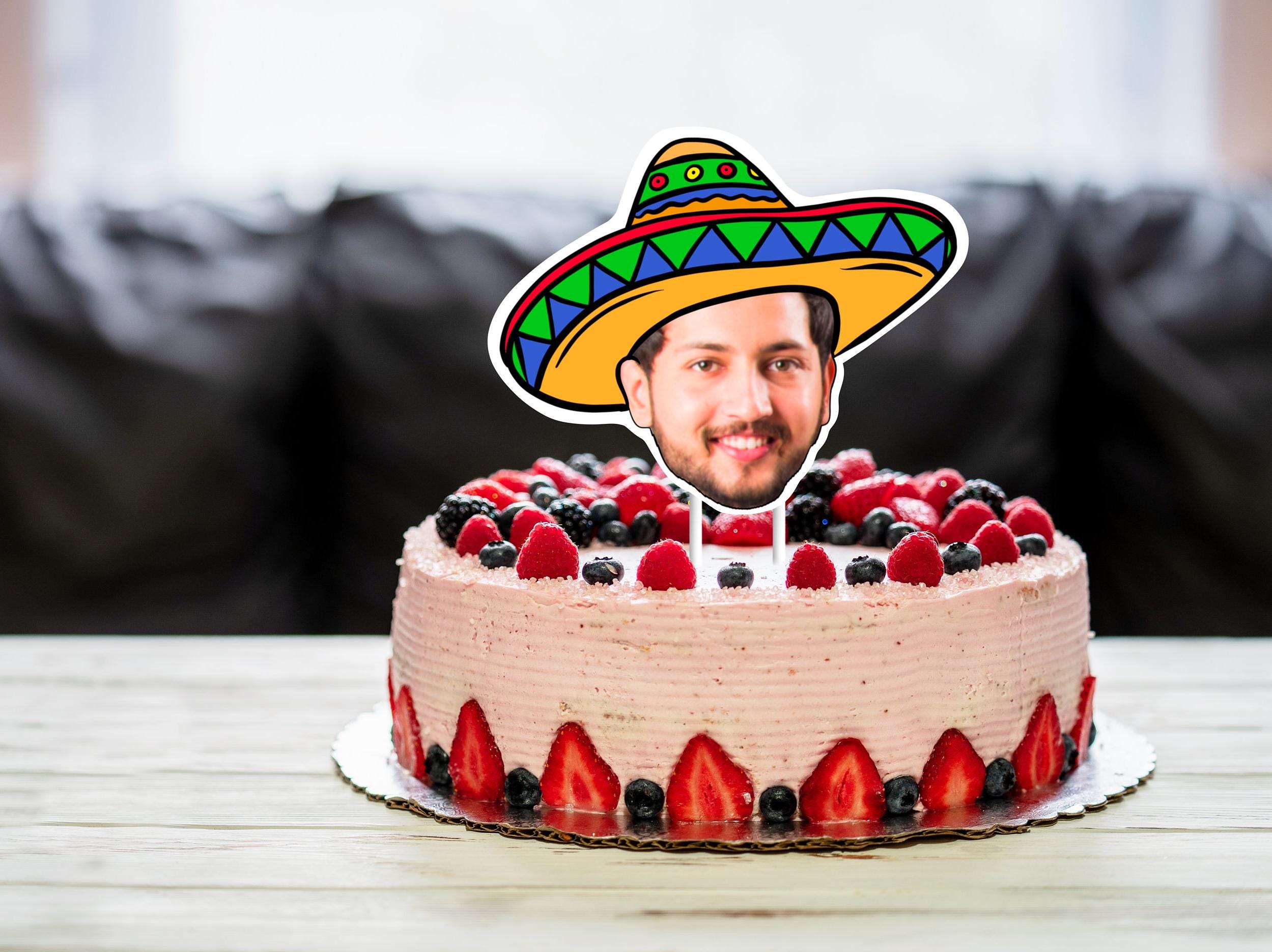 A personalised cake topper featuring a cut-out photo of a persons head, with a vibrant and colourful sombrero placed on top. The sombrero adds a playful and festive element to the cake, making it a fun and unique centrepiece for any celebration.