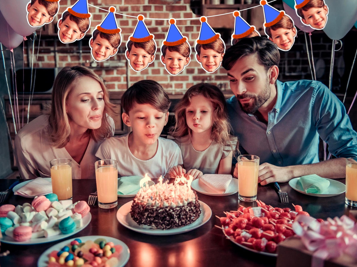 Family birthday celebration with custom face banner featuring a child in blue party hat with orange trim. Banner hangs above cake as family blows out candles. Perfect personalised party decoration.