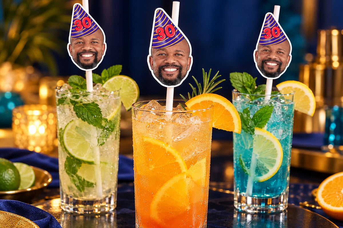 Text-free close-up of 30th birthday photographic head toppers on white paper straws in tall glasses.